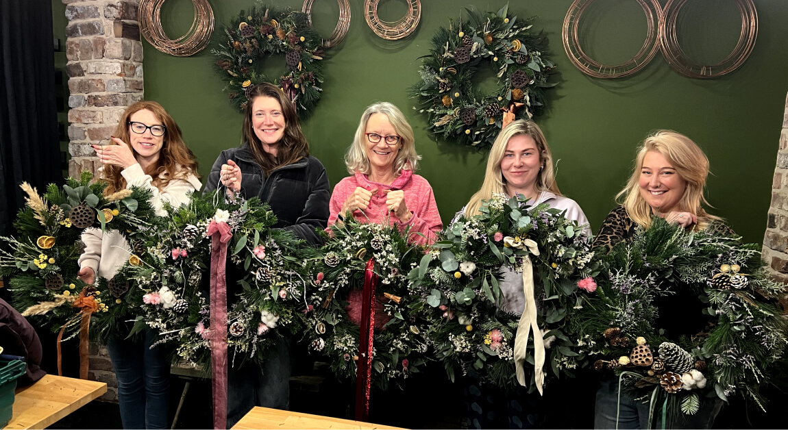 A group of workshop attendees show off their completed Christmas wreaths